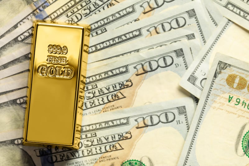 gold bar on top of 100 dollar bills